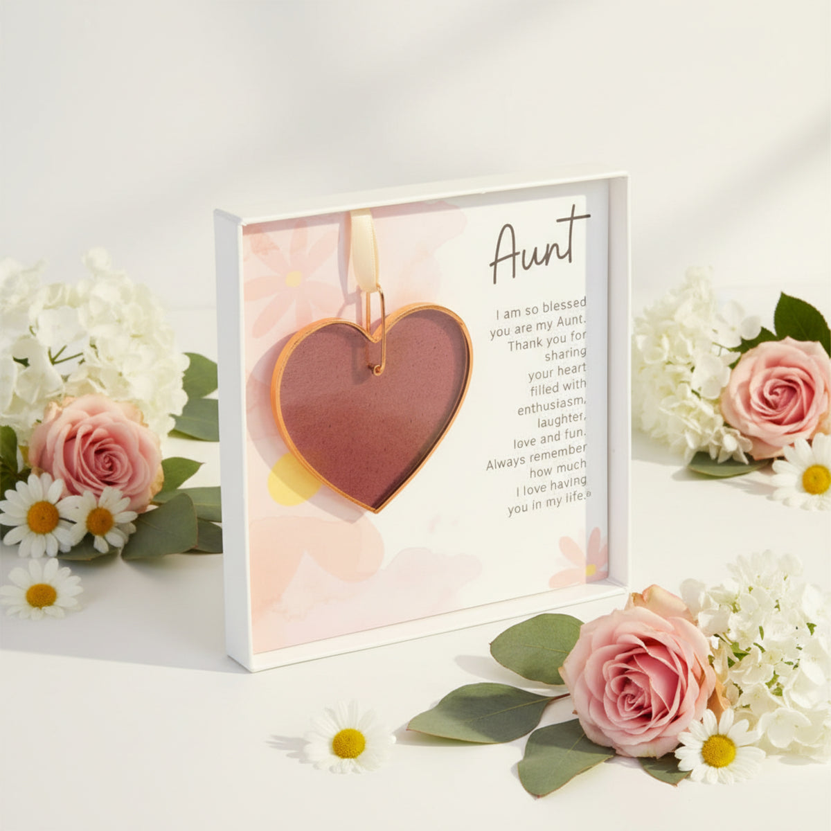 Pink rose mauve glass heart with Aunt sentiment in a white box with clear lid with a white background surrounded by flowers.