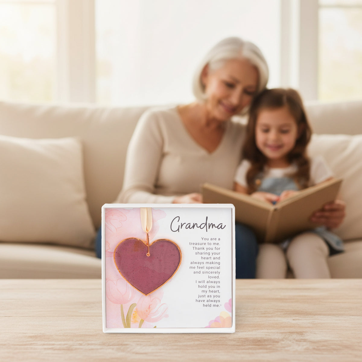 Grandma gift on a table with a granddaughter and her grandma in the background reading a book together.
