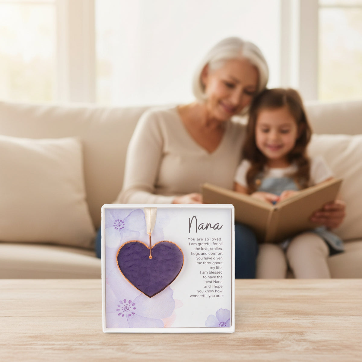 Nana gift on a table with a granddaughter and her nana in the background reading a book together.