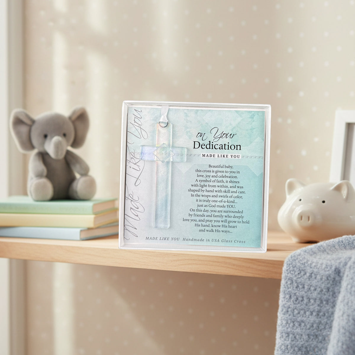 "On Your Dedication" glass cross gift on a shelf in a baby's room.