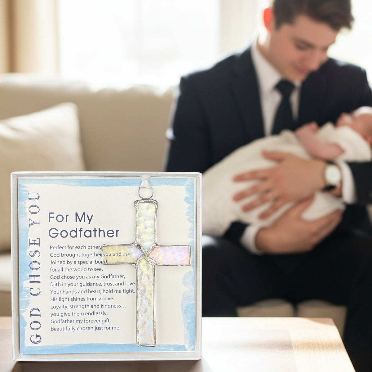 Godfather gift on a table with a Godfather holding his godchild in the background.