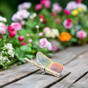 2 of 5:Stained glass butterfly on a wooden table with flowers in the background.