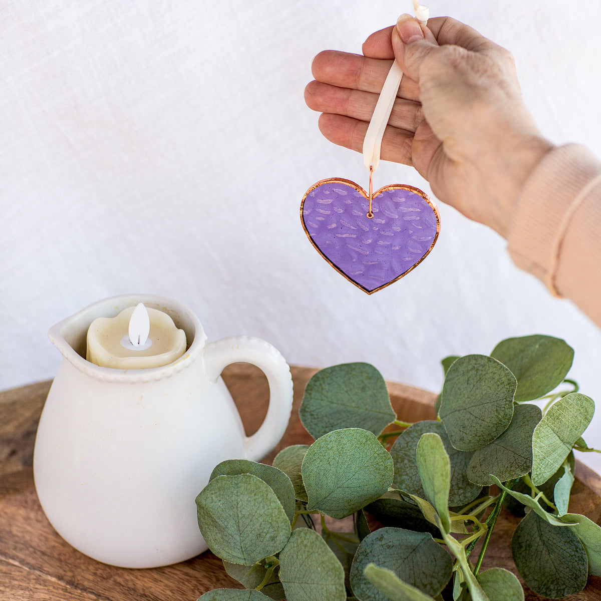 Purple stained glass heart being suspended by a hand allowing the light to shine through and show the color of the glass.