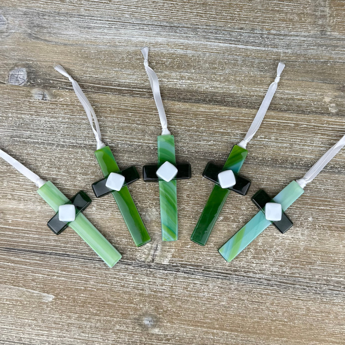 An assortment of 4" glass crosses made with green glass in shades of green and blue. Include a satin ribbon for hanging.
