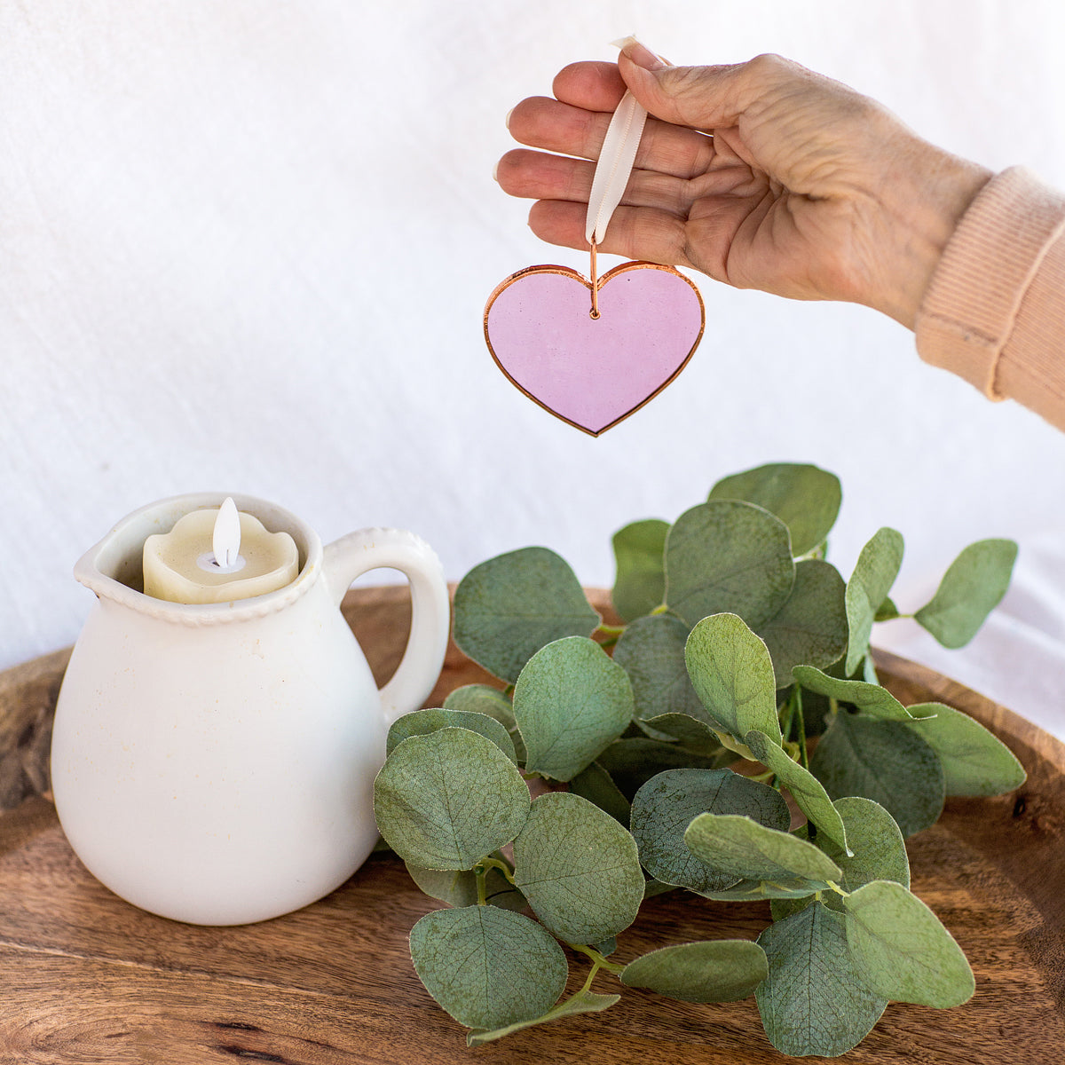 Pink rose mauve stained glass heart being suspended by a hand allowing the light to shine through and show the color of the glass.