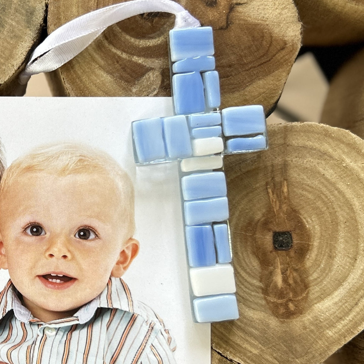 4" mosaic glass cross in shades of blue and white with a white satin ribbon for hanging.