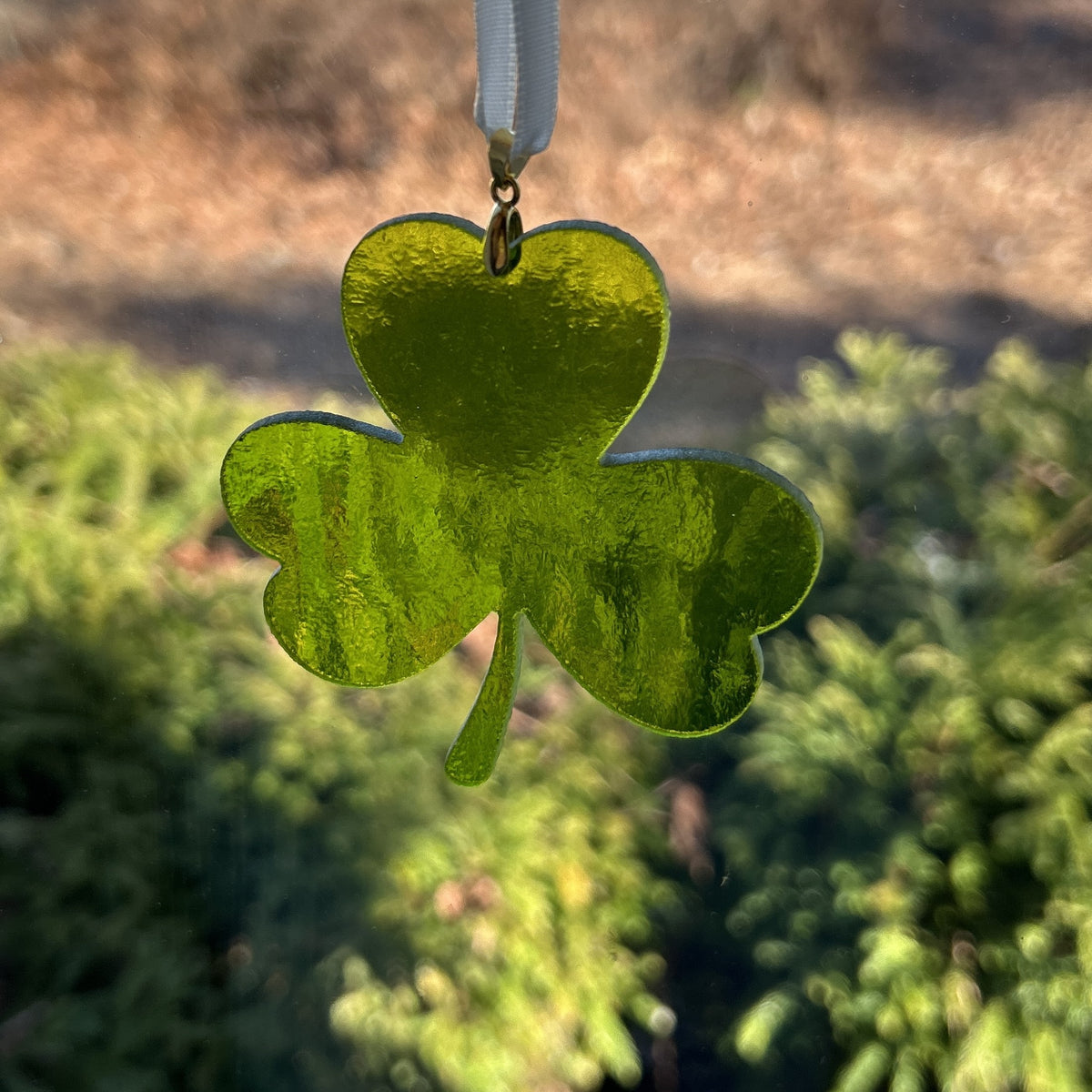 Stained glass shamrock hanging in a window showing the texture of the glass.