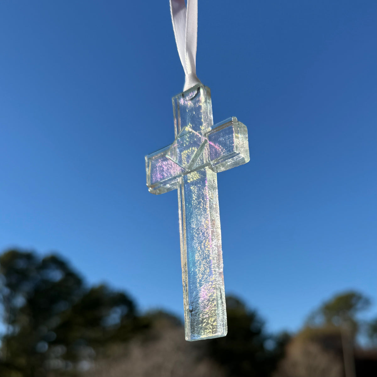 Clear iridescent cross hanging in the sunlight to show how the light reflects color in the glass.