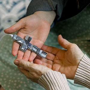 4 of 7:Hands exchanging a gray mosaic cross.
