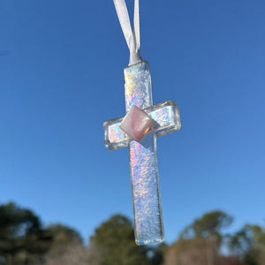 3 of 4:Clear Iridescent Cross with Pink accent hanging in the sunlight showing the beauty of the glass.