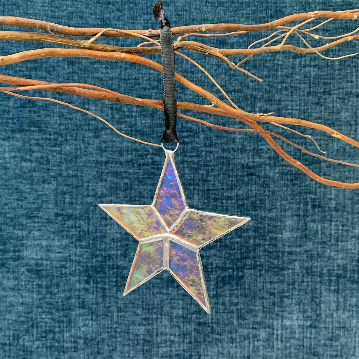 Clear iridescent stained glass star with silver edging hanging from black satin ribbon.