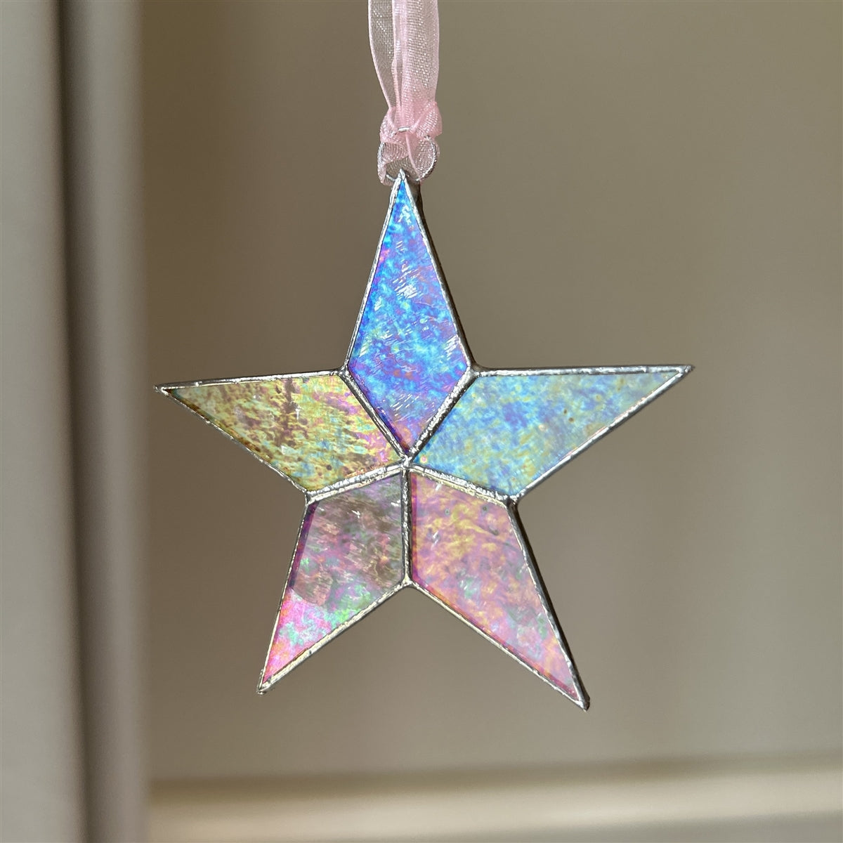 Clear iridescent star hanging from a pink organza ribbon.