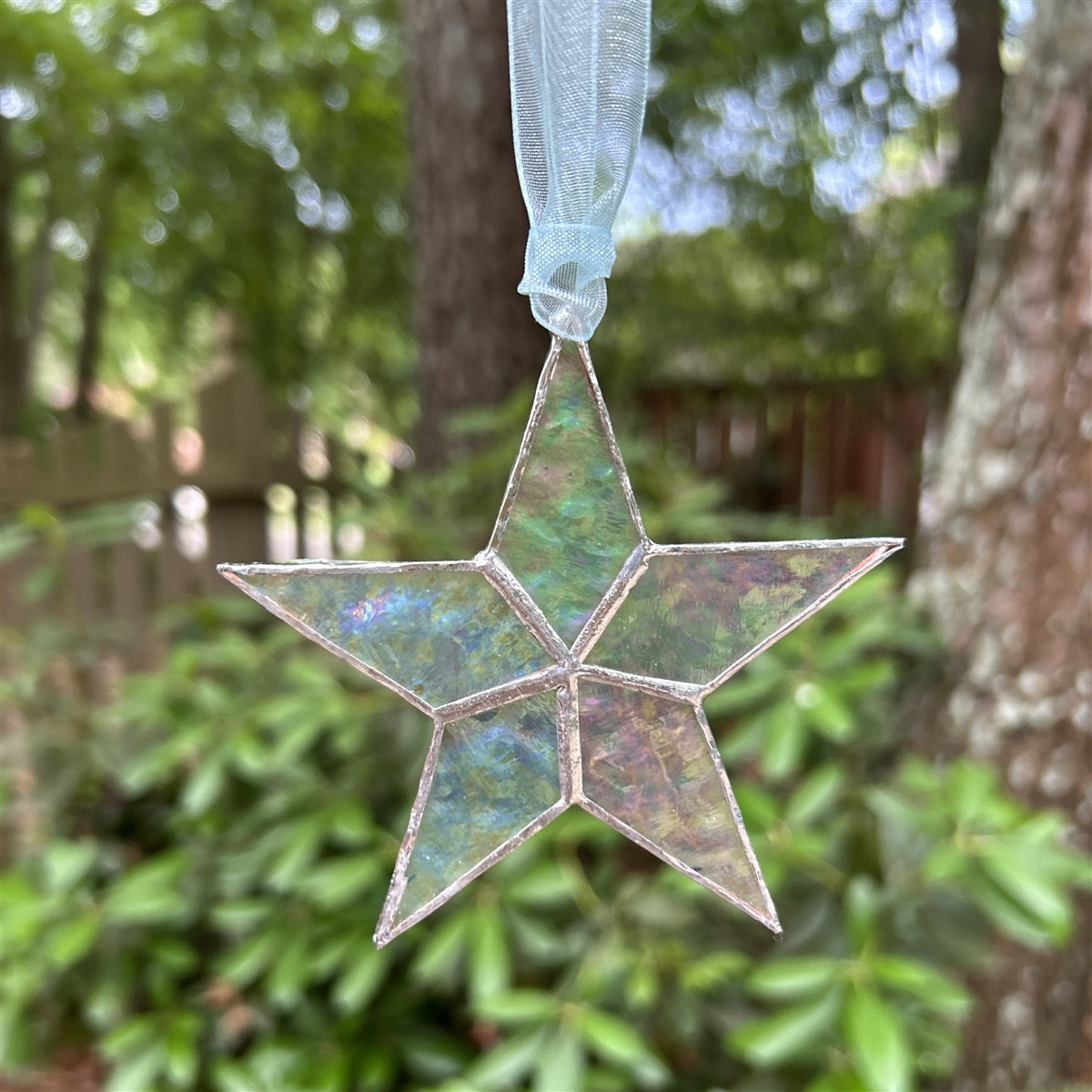 Clear iridescent star hanging from blue organza ribbon..