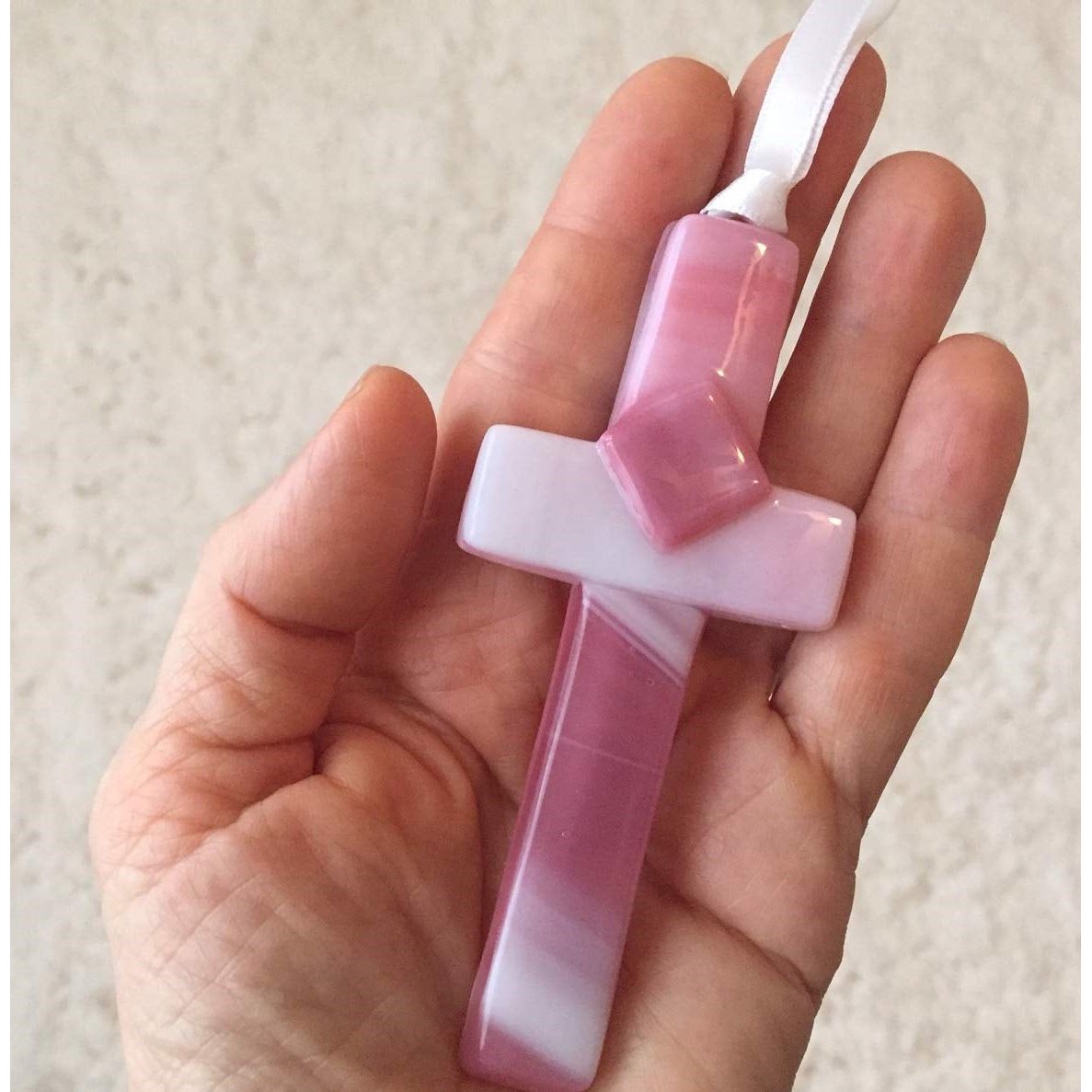 Pink glass cross being held in a hand.