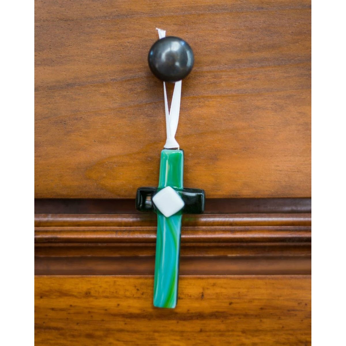 Green glass cross with white satin ribbon for hanging.