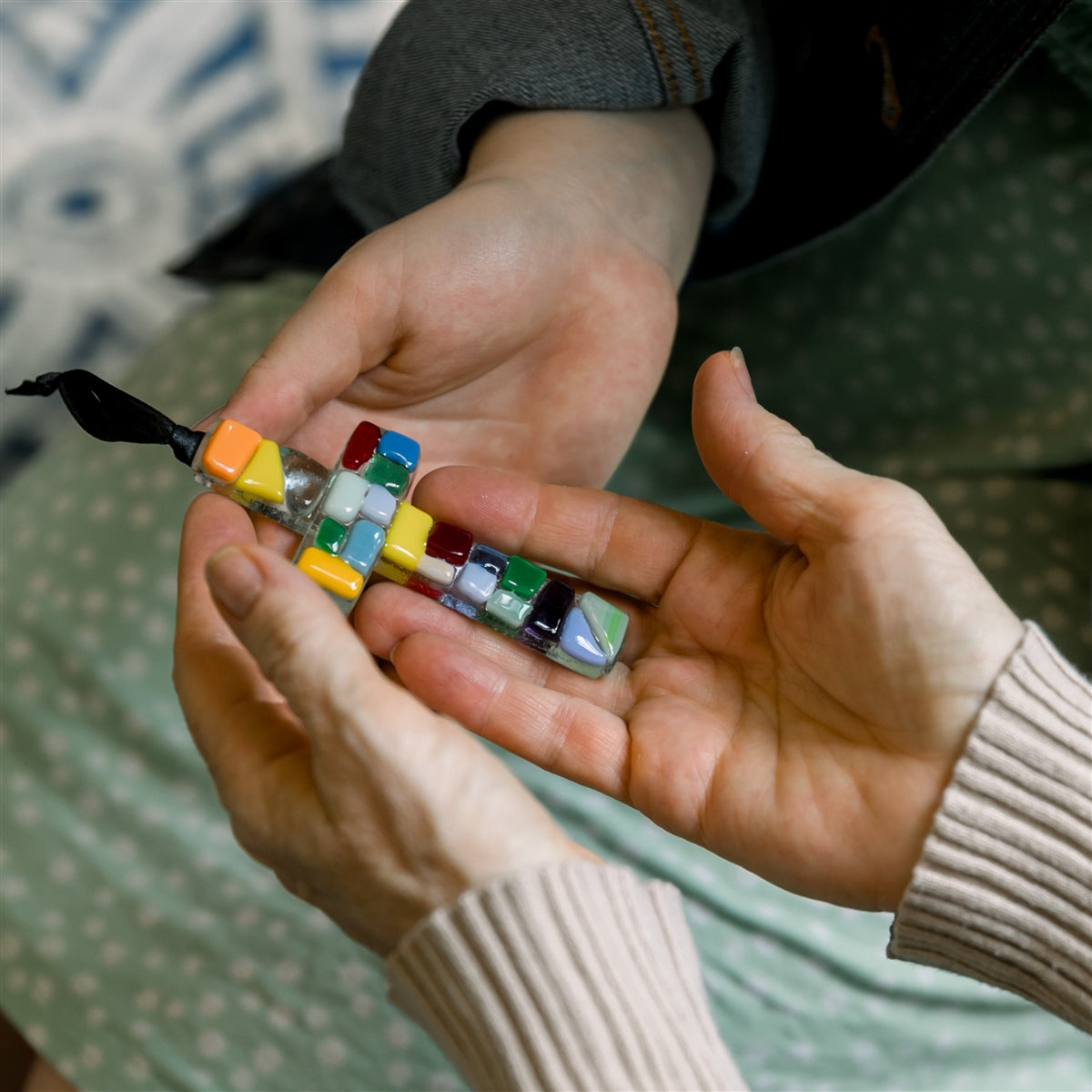 Multi-colored glass mosaic ornament being exchanged between two sets of hands.