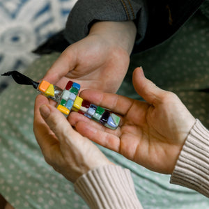 4 of 5:Multi-colored glass mosaic ornament being exchanged between two sets of hands.