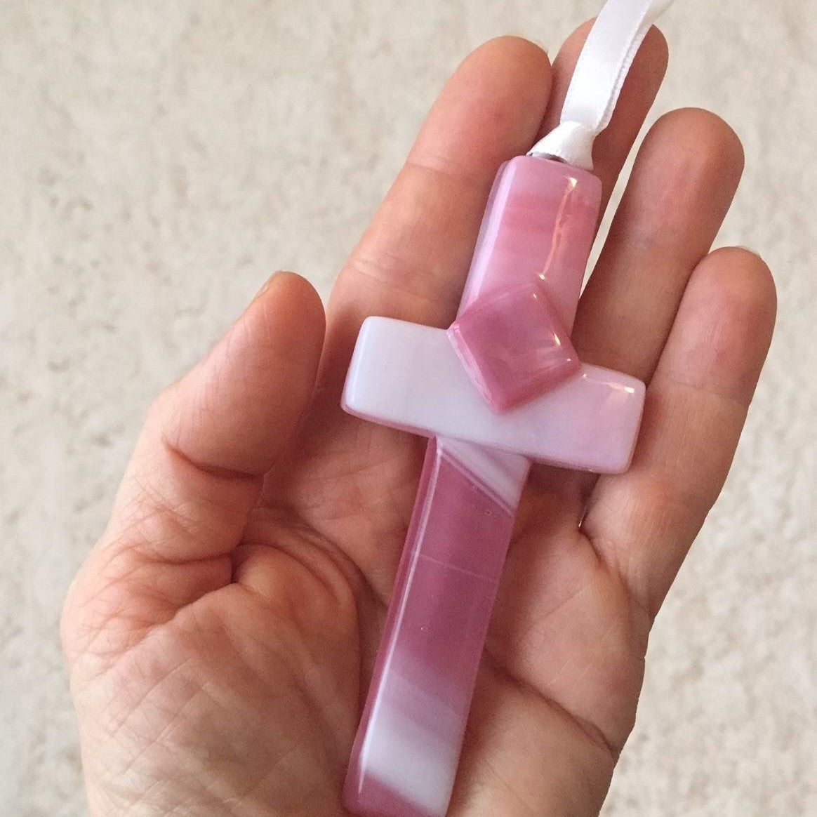 Pink glass cross being held in a hand.