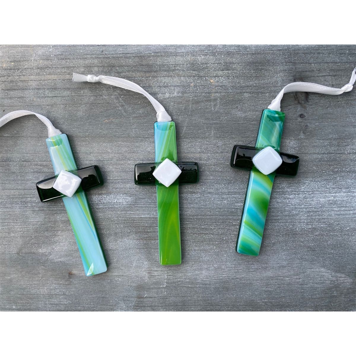 An assortment of green glass crosses with swirls of green and blue.