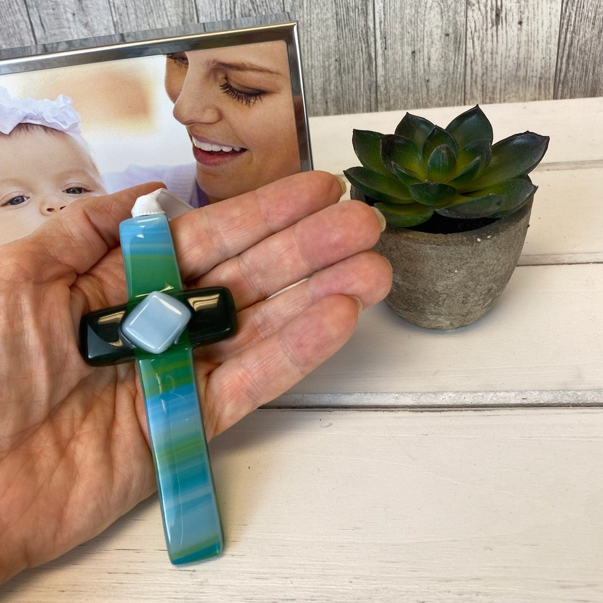 Green glass cross being held in a hand.