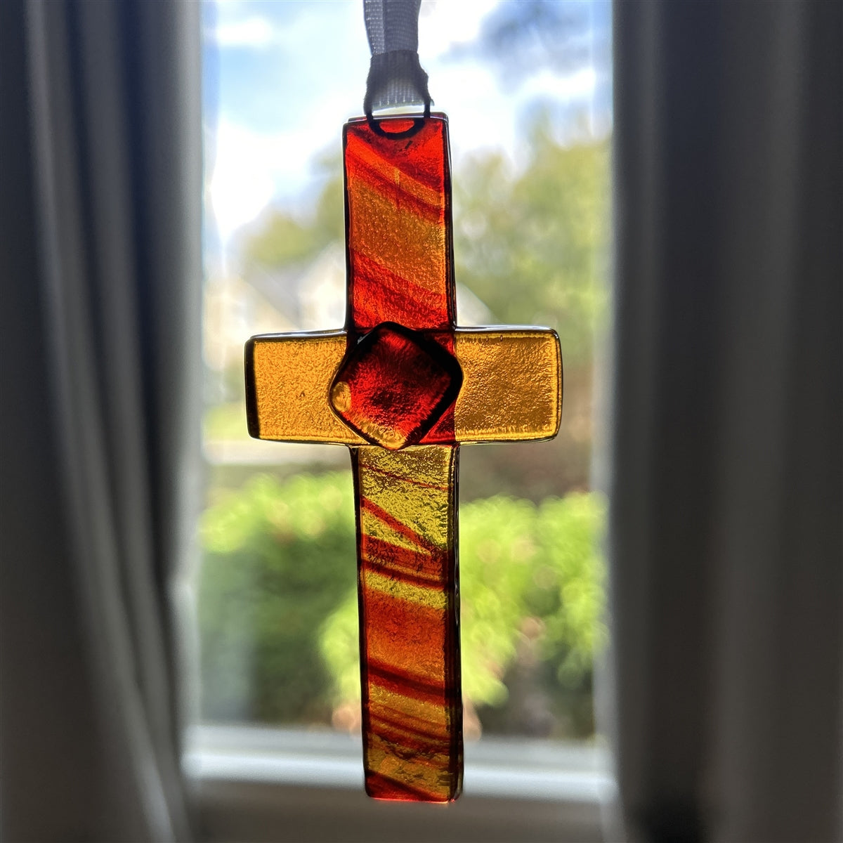 Glass cross with the light shining through to show the swirls of amber and brown in the glass.