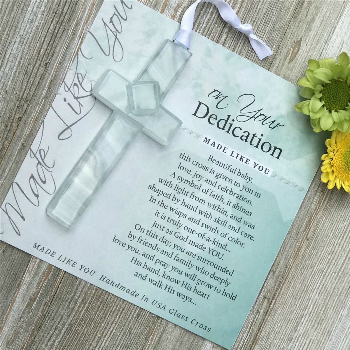 Clear glass cross with swirls of white lying on the "On Your Dedication" sentiment artwork.