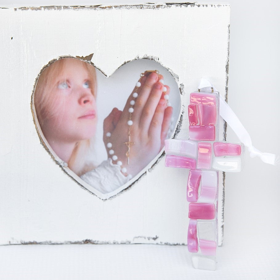 A pink mosaic cross with white satin ribbon for hanging.