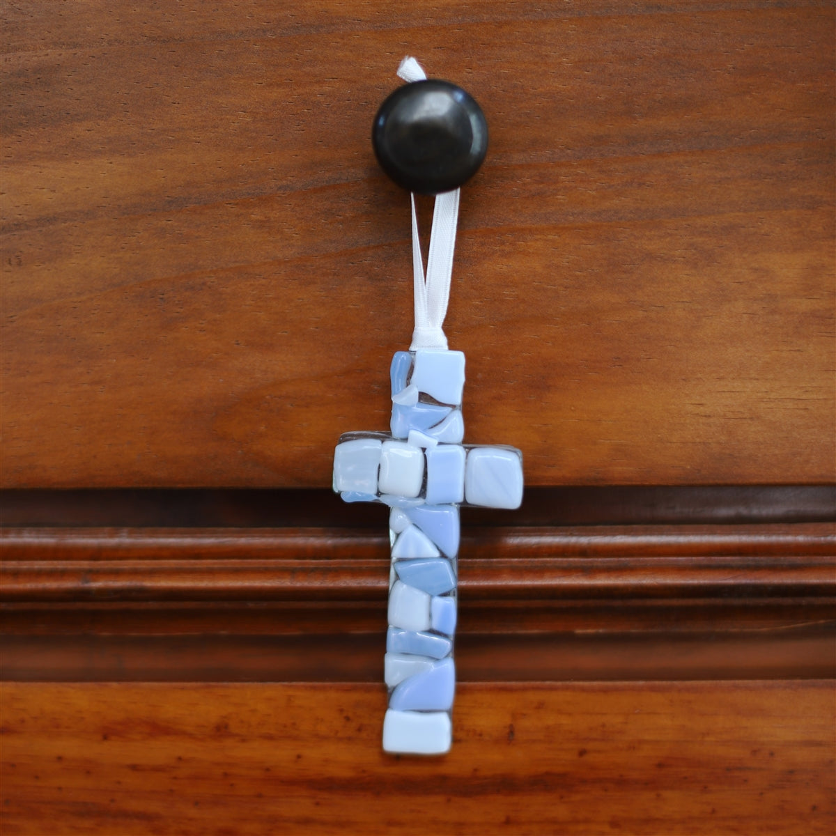 A blue mosaic cross with white satin ribbon for hanging.