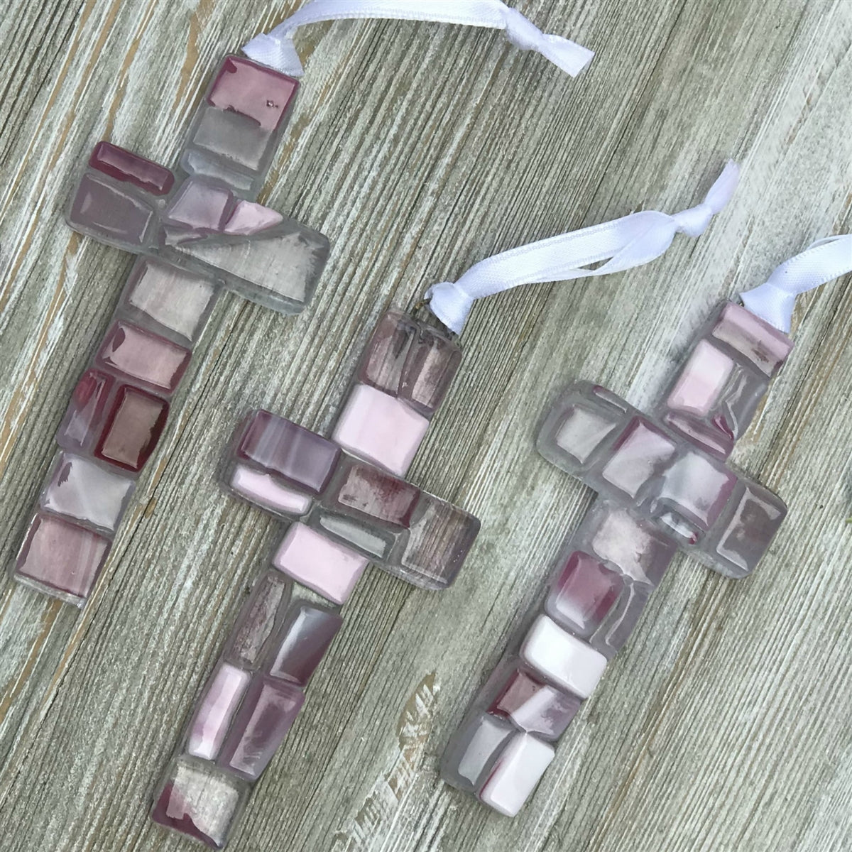 An assortment of pink mosaic crosses with varying shades of pink, white, and clear glass.