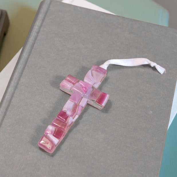 Pink mosaic glass cross laying on a book.