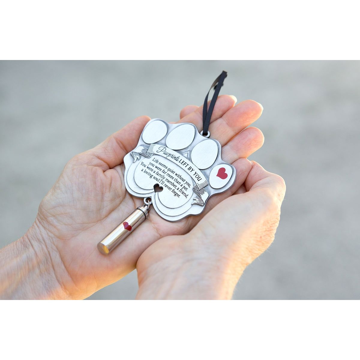 Pawprints Left By You ash vial ornament being held in a hand.