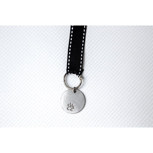 5 of 6:Up close view of engravable pawprint tag hanging by black grosgrain ribbon with white edge stitching.