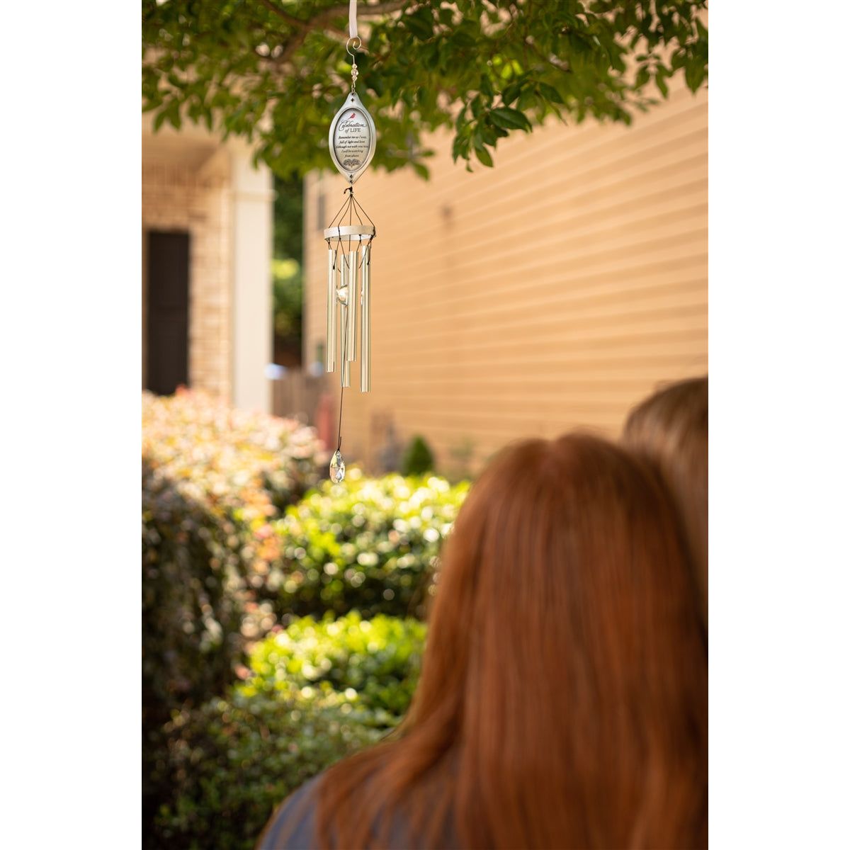 Two women admiring the windchime hanging in a tree.