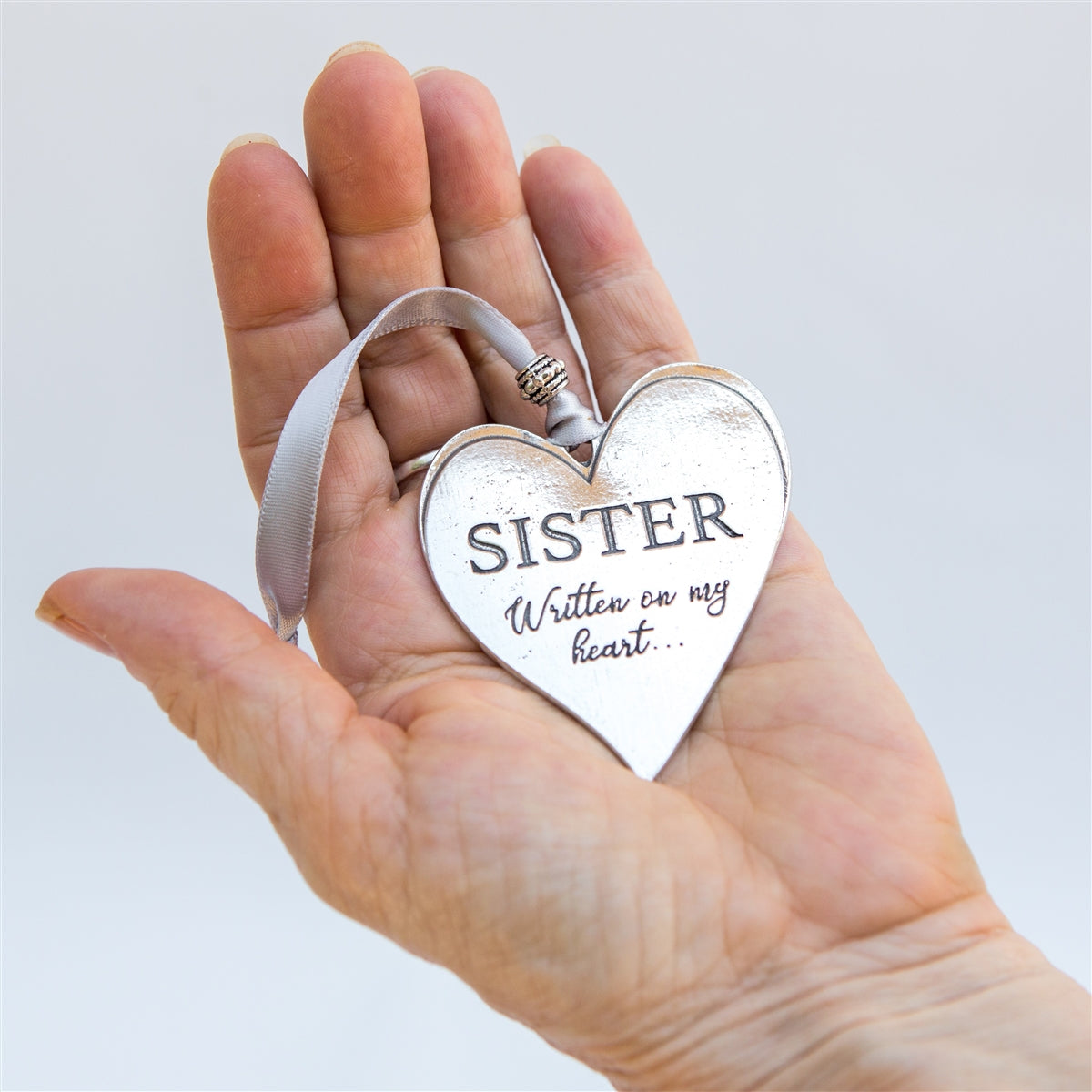 Cast pewter heart engraved with "Sister Written on my heart" held in a hand.