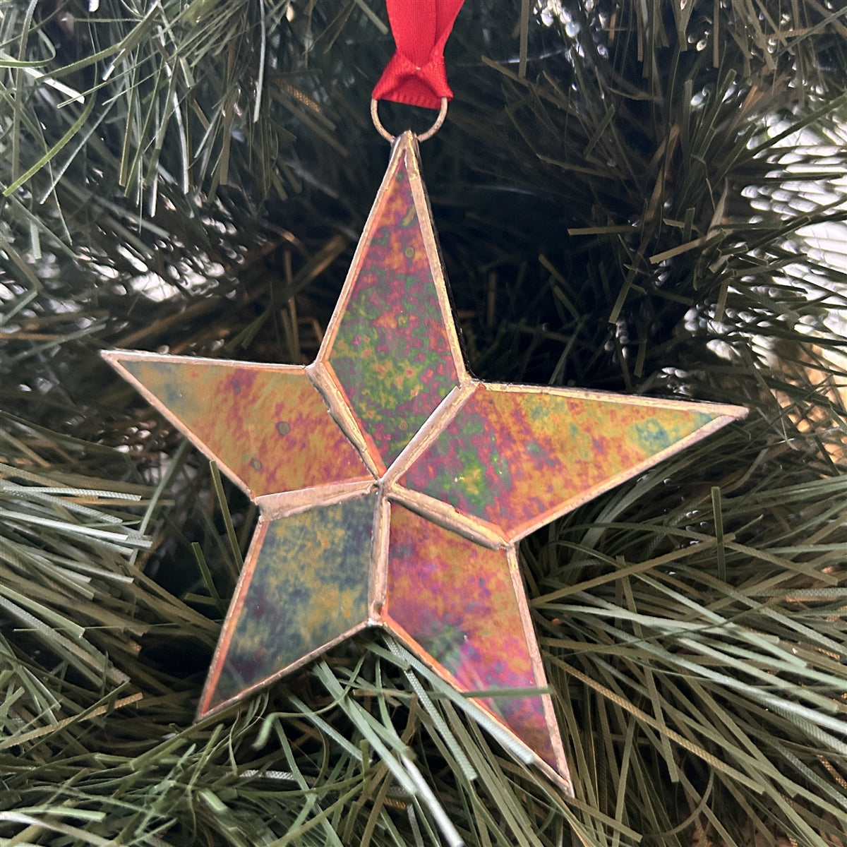 cCear iridescent stained glass star with silver edging hanging from red satin ribbon.