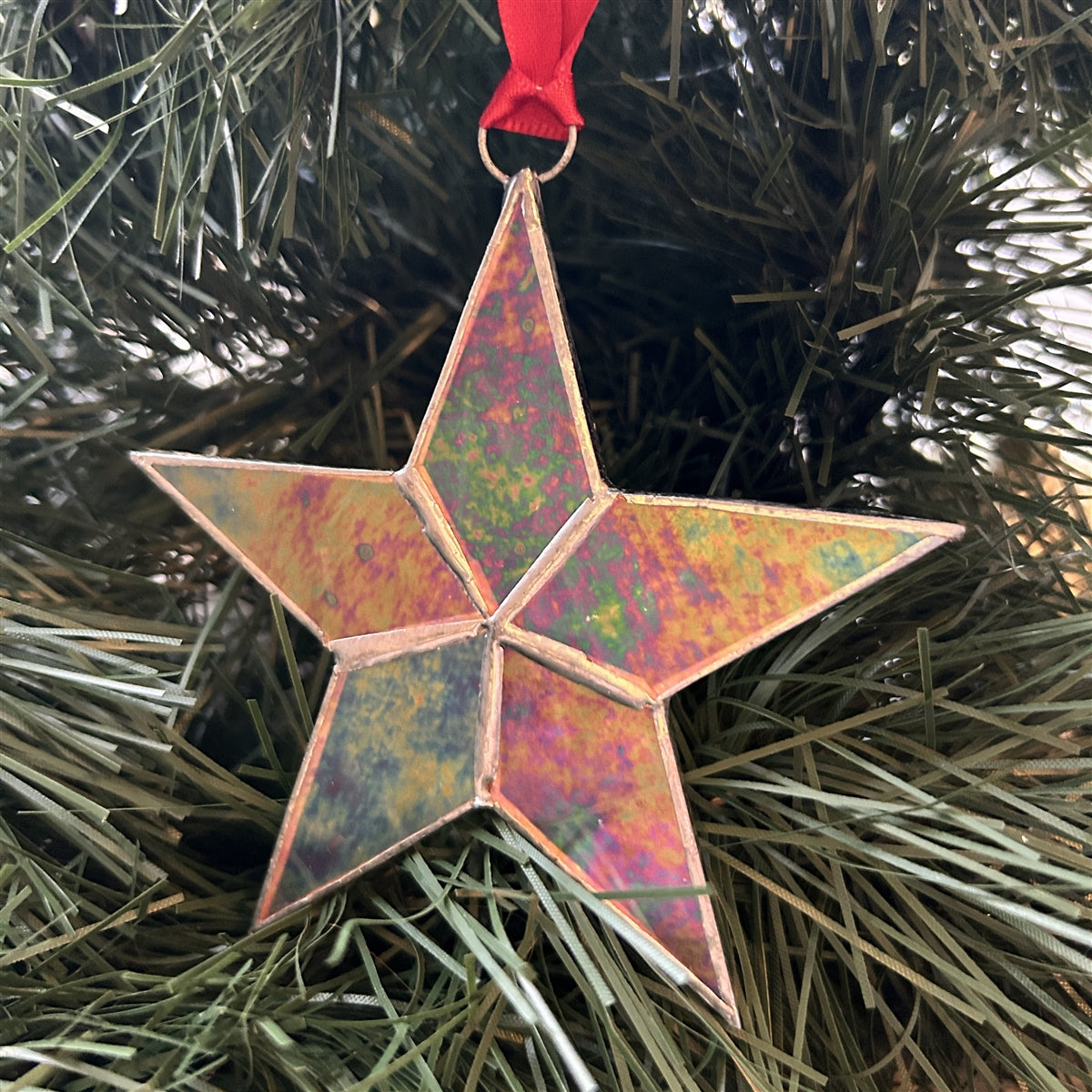 Clear iridescent stained glass star with silver edging hanging from red satin ribbon.