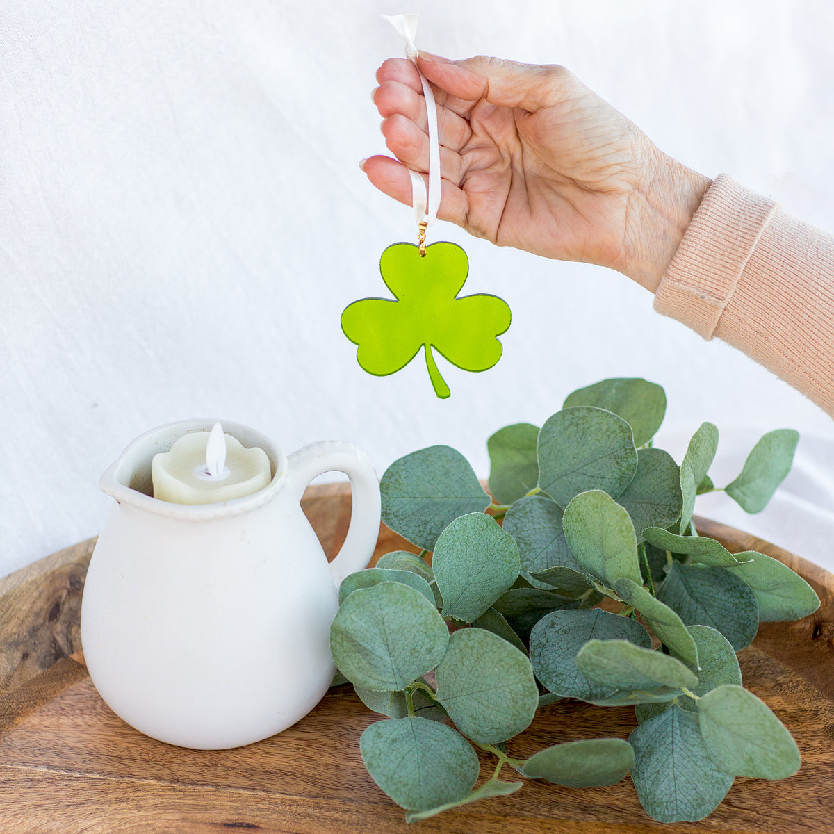 A glass shamrock being held by a hand showing the light shining through the glass.