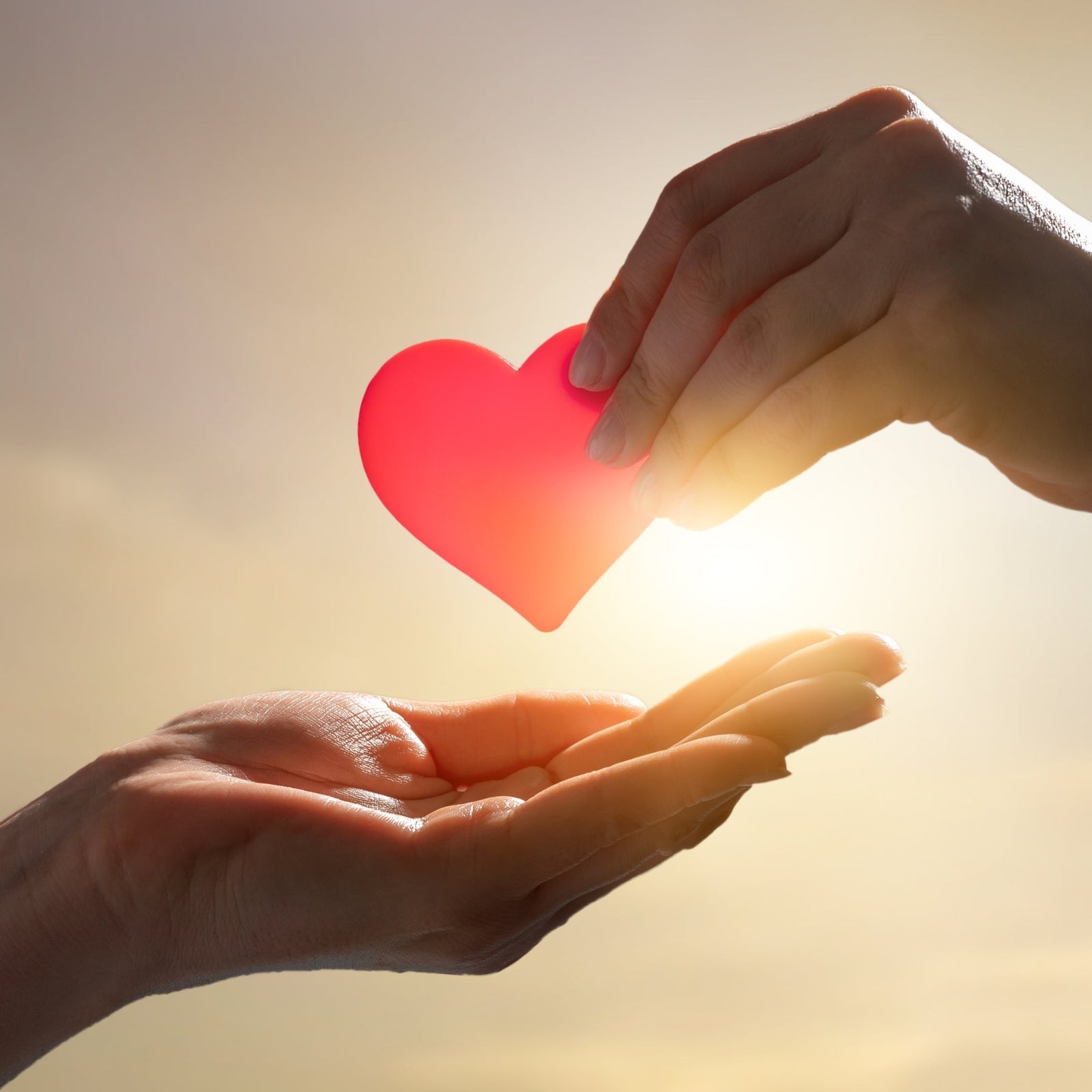 A red glass heart being held in the sunlight.