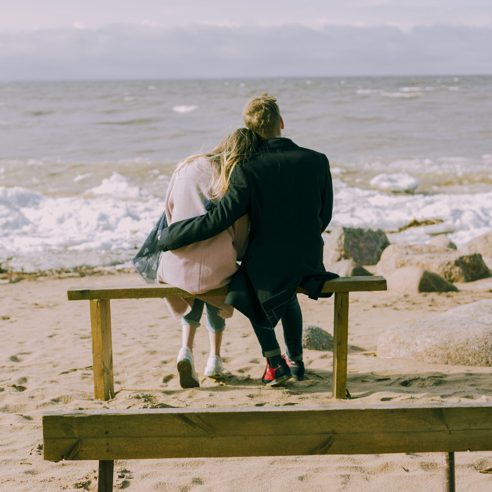 Two people sitting on a bench looking at the ocean.
