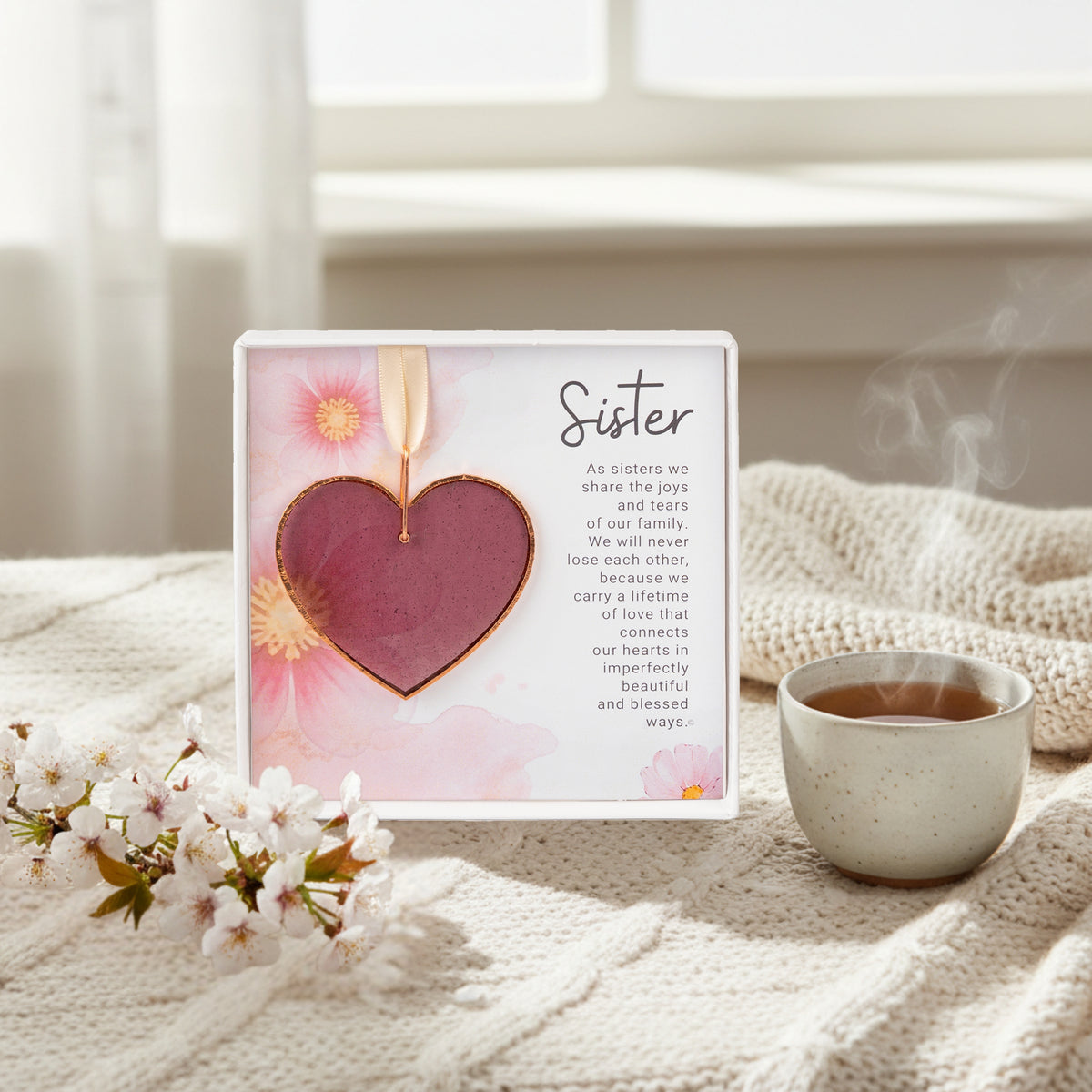 Sister gift sitting on a throw next to coffee and some flowers.