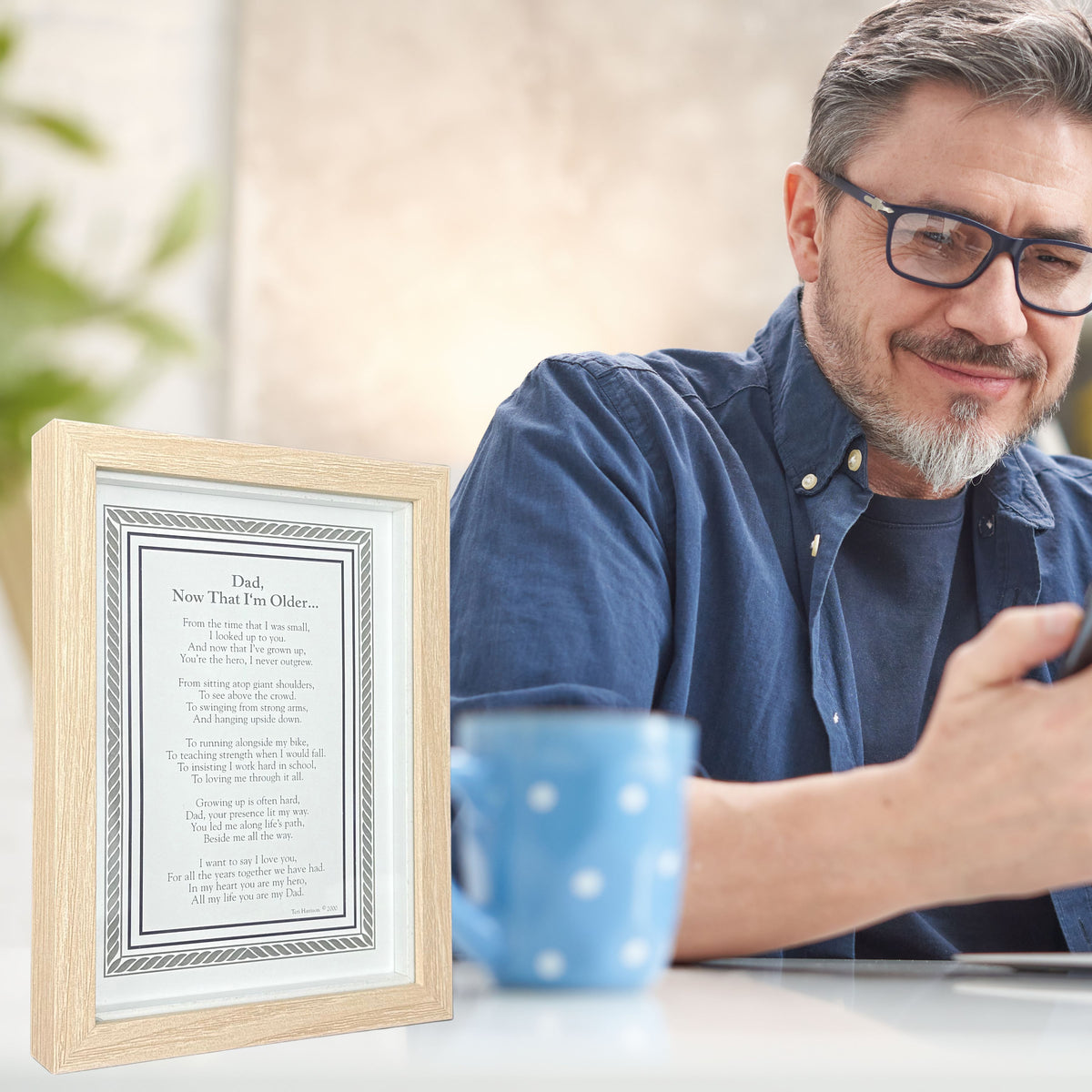 Man sitting at a table with &quot;Dad, Now that I&#39;m Older&quot; framed poem.