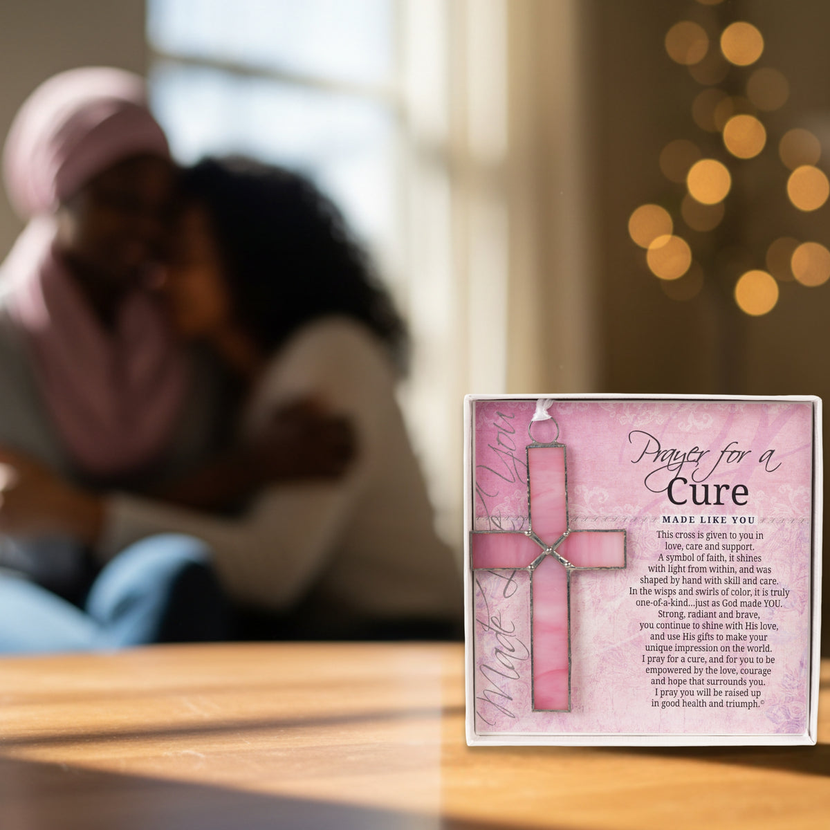 "Prayer for a Cure" cross on a table with friends embracing in the background.