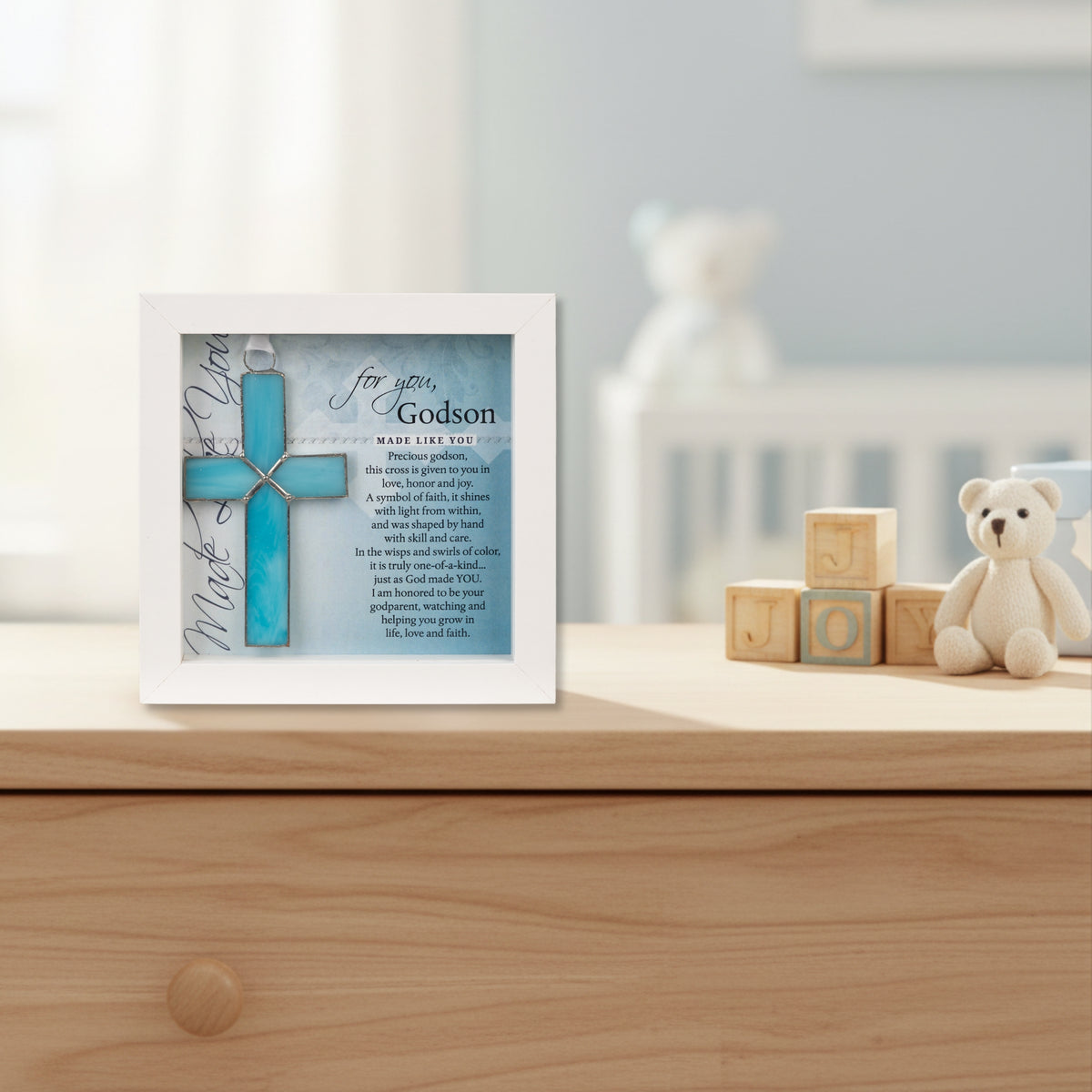 Framed light blue cross with "For you, Godson" Sentiment on a dresser in a boy's nursery.