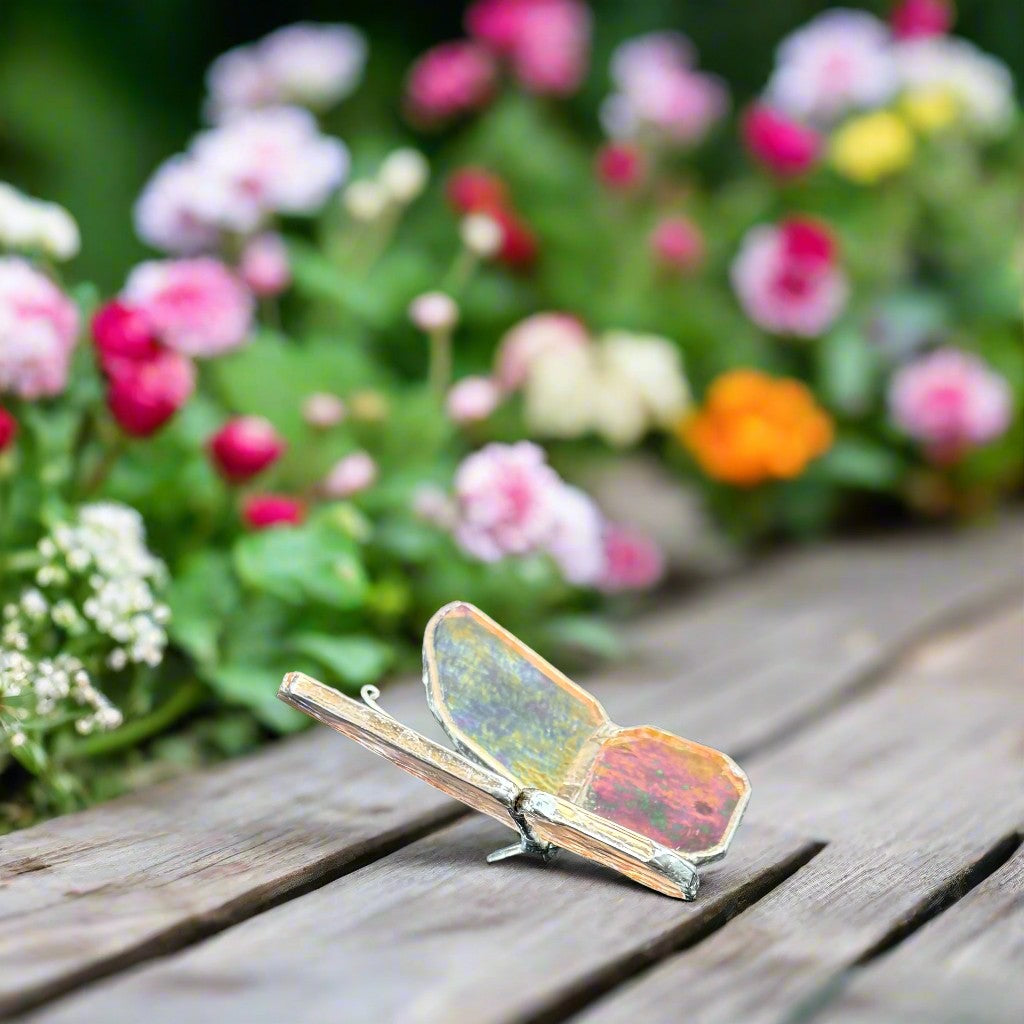 Stained glass butterfly on a wooden table with flowers in the background.