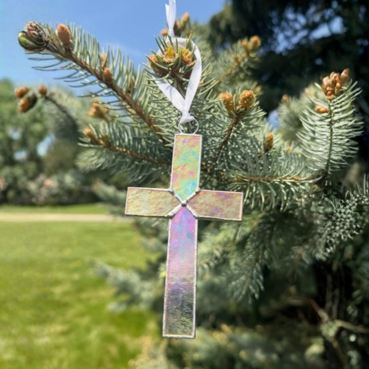 Clear iridescent cross hanging in the sunlight to show how the light reflects color in the glass.