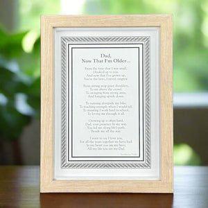 1 of 8:5x7 framed poem titled 'Dad, Now That I'm Older' on a wooden table in front of a garden window.