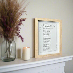 3 of 5:Framed poem titled 'Daughter Now That You're a Mother' on a mantelpiece with a candle and vase of dried flowers.