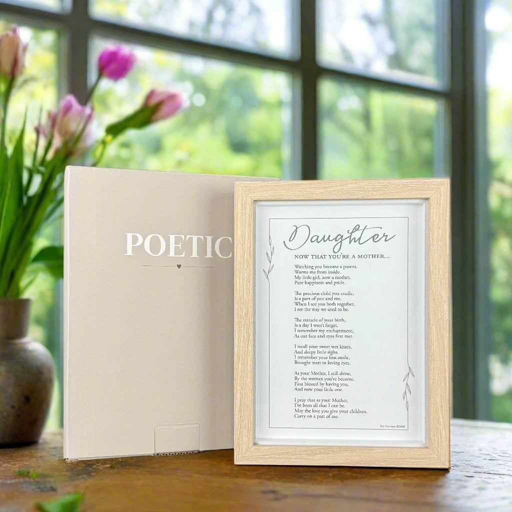 Framed poem in front of its box on a table with flowers in the background.