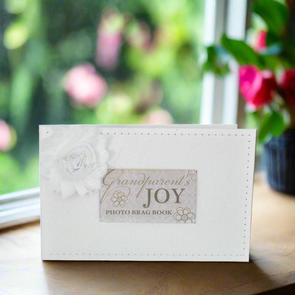 White photo brag book titled &#39;Grandparent&#39;s Joy&#39; on a surface with a blurred floral background.