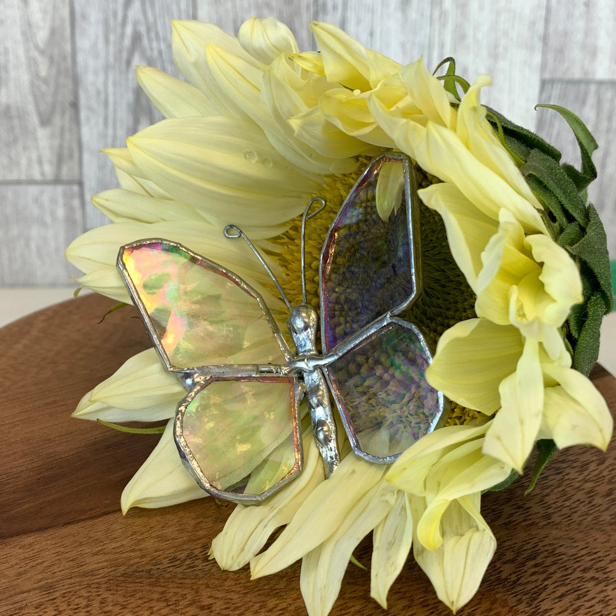 Stained glass butterfly resting on a yellow flower.